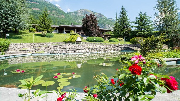 A serene hotel setting with a pond, lush greenery, and a mountain backdrop.