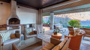 A covered outdoor seating area with wicker furniture, a stone fireplace, and a view of mountains.