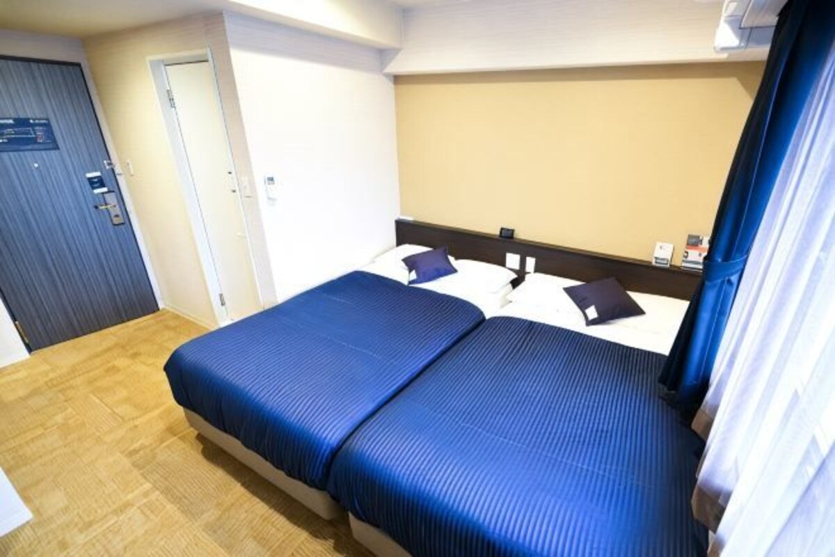 A hotel room with a double bed, a wooden floor, a door, and a wall-mounted light fixture.