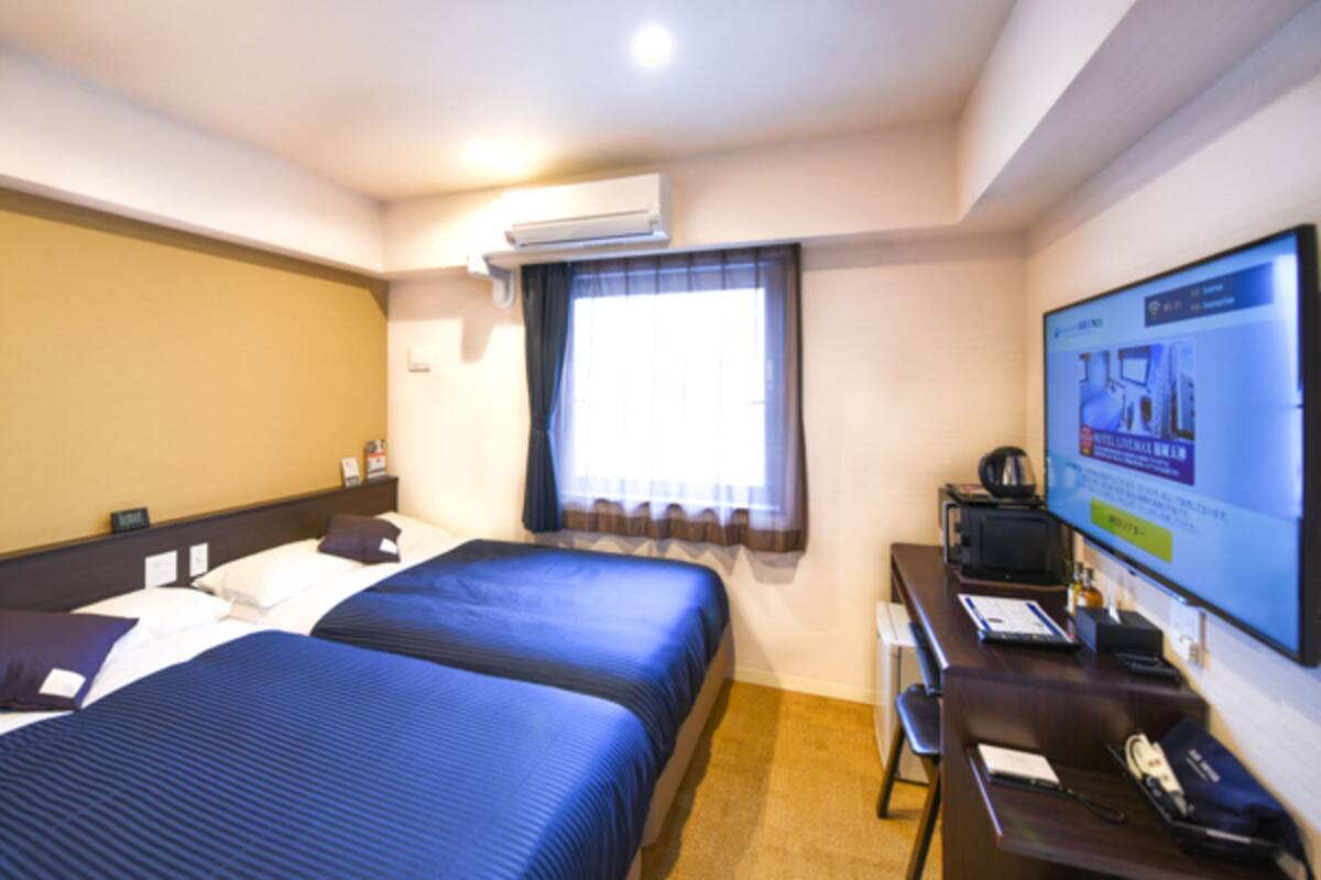 A hotel room with two beds, a desk, a chair, a television, and an air conditioning unit.