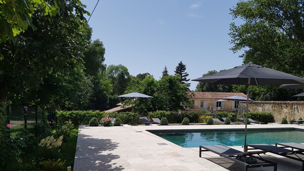 A swimming pool with lounge chairs and umbrellas, surrounded by greenery and a stone building. - House / Villa - Clermont de Beauregard (Clermont-De-Beauregard)