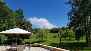 An outdoor seating area with a table and chairs, a white umbrella, and a view of a green landscape with trees and a hill. - House / Villa - Clermont de Beauregard (Clermont-De-Beauregard)