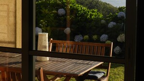 A patio with a wooden table and chairs, a hanging light fixture, and a view of a coastal landscape with greenery and a body of water.