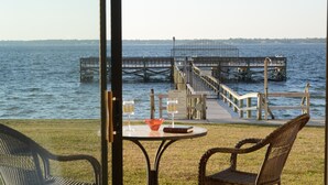 A view from a balcony overlooking a body of water, featuring a wooden dock, a glass table with two chairs, and a glass of wine. - "Julie's Jewel"  - A Real Gem - Perfect for A Couple! (Navarre)