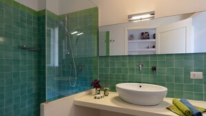 Ein Badezimmer mit einem weißen Waschbecken, grünen Fliesen, einer Glasdusche und einem Spiegel über dem Waschbecken.