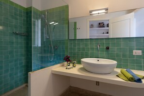 A bathroom with a white sink, green tiles, a glass shower enclosure, and a mirror above the sink. - Charming house with stunning sea views over the bay of Sampieri, Sicily 6 people (Sampieri)