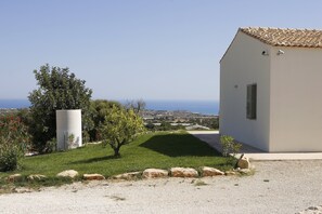 A modern house with a white exterior and a tiled roof, situated on a grassy slope overlooking a coastal landscape.
