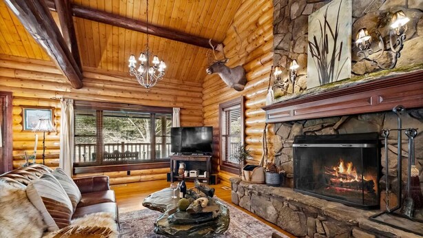 A log cabin interior with a stone fireplace, leather furniture, and a mounted deer head. - Cinnamon Valley - The Cattail (Eureka Springs)