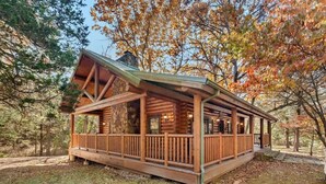 A log cabin with a porch, surrounded by trees with autumn foliage. - Cinnamon Valley - The Cattail (Eureka Springs)