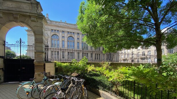 A courtyard with bicycles parked near an archway, surrounded by greenery and a building with classical architecture. - Apartment/ flat - Strasbourg (Strasbourg)