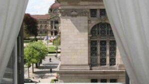 A view through a window with white curtains, featuring a historic building with a prominent archway and a statue on top. - Apartment/ flat - Strasbourg (Strasbourg)