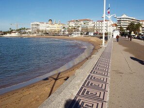 Un paseo marítimo con un camino de diseño, edificios frente a la playa y un cielo despejado.