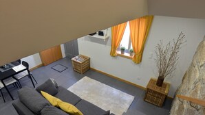 Un soggiorno moderno con un divano grigio, un tavolino, una finestra con tende arancioni e un muro in pietra.