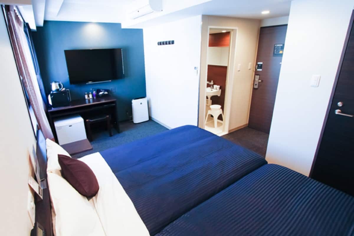 A hotel room with a bed, a desk, a TV, a mini-fridge, and a bathroom.