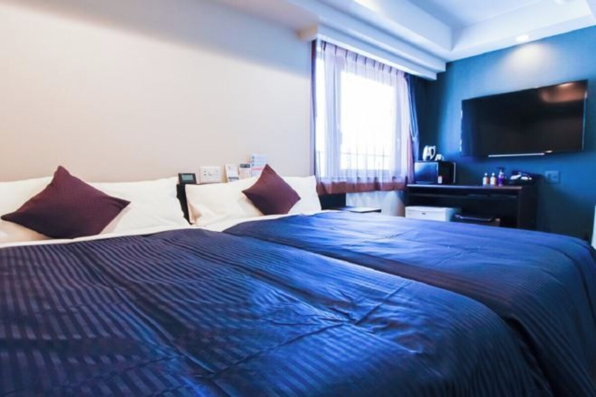 A hotel room with a large bed, a flat-screen TV, and a window with curtains.