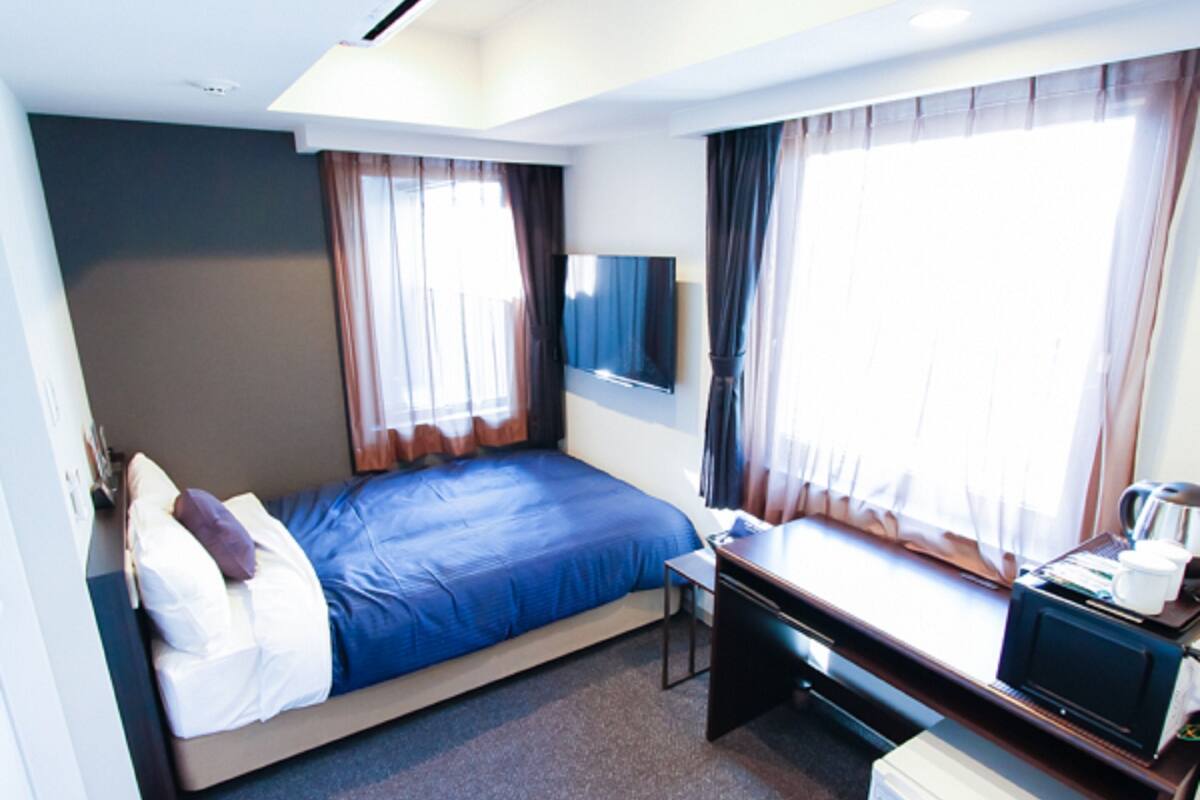 A hotel room with a bed, a desk, a chair, a television, and a window with curtains.