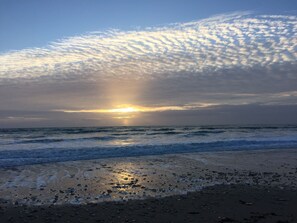 A beach with the sun setting over the ocean, creating a silhouette of clouds.