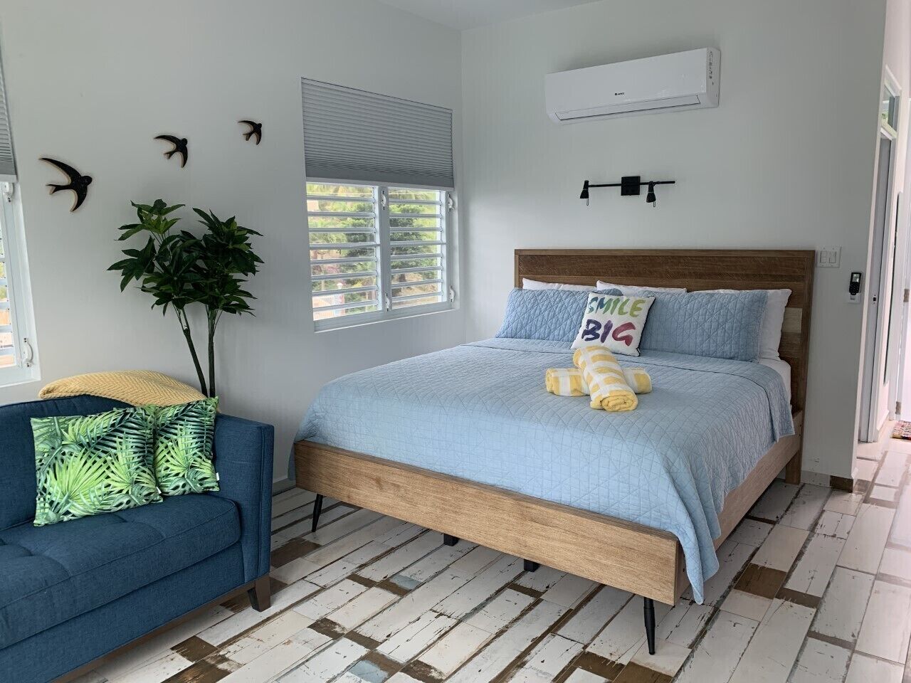 A bedroom with a bed, a blue sofa, a potted plant, and a window with blinds.