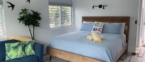 A bedroom with a bed, a blue sofa, a potted plant, and a window with blinds.