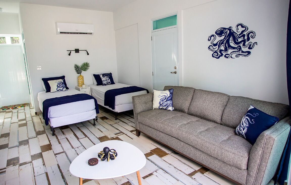 A room with a sofa, two beds, a small table, and a decorative wall piece.