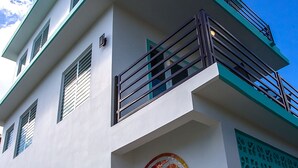 Een gebouw met een witte gevel, een balkon met metalen hekwerk, en een logo met de tekst 'THE BEACH PAD'.