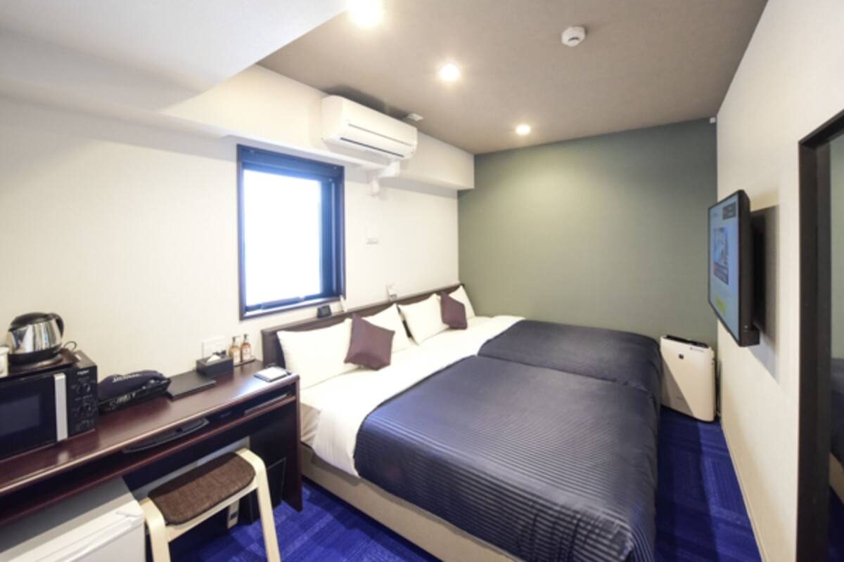 A hotel room with a bed, desk, chair, and a television.