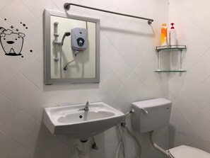 A bathroom with a white sink, toilet, and a shower with a handheld showerhead. There is a glass shelf with toiletries and a mirror above the sink. - Langkawi Destaz (Langkawi)