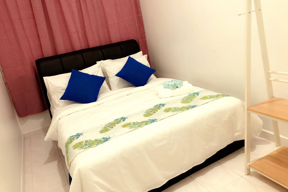 A neatly made bed with white and blue bedding, a wooden nightstand, and a white chair.