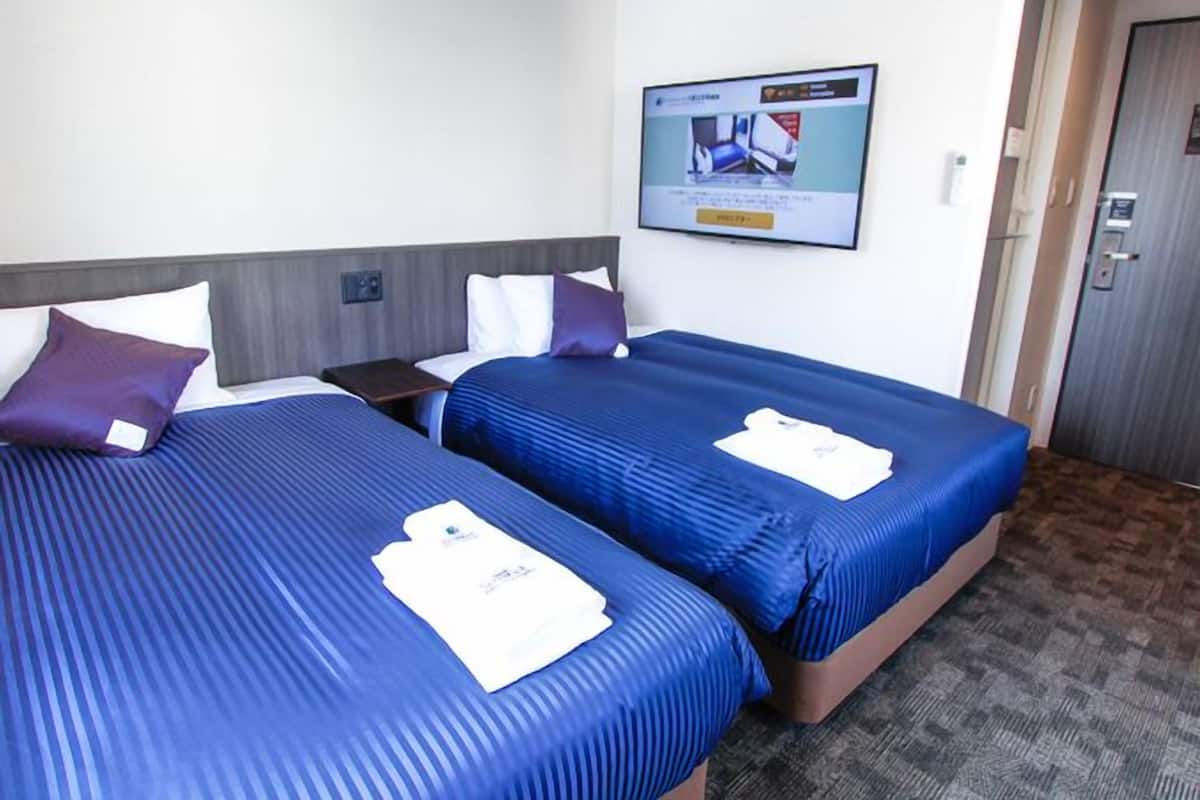 A hotel room with two beds, a flat-screen TV mounted on the wall, and a door to the right.