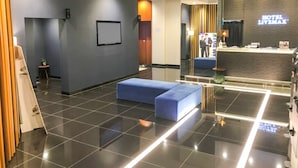 A modern hotel lobby with a reception desk, a blue seating area, and a large mirror reflecting the space. - Hotel Livemax Osaka Yodoyabashi (Osaka)