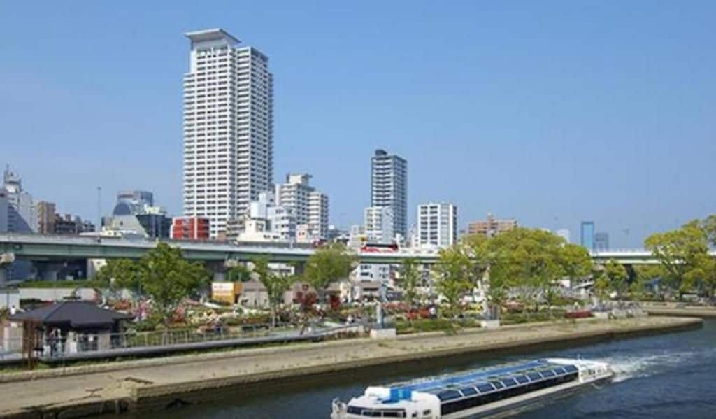 Un río con un bote, un puente y el horizonte de una ciudad con edificios altos.
