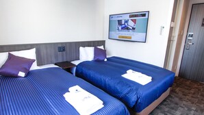 A hotel room with two beds, each with a blue bedspread and white pillows. There is a small table between the beds, and a television mounted on the wall. - Hotel Livemax Osaka Yodoyabashi (Osaka)