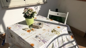 Een tafel met een tafelkleed met bloemen, een potplant en een stenen kom op een betegelde vloer.