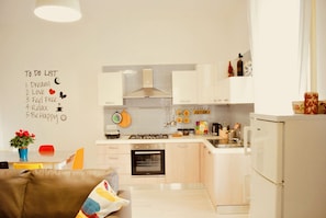 A modern kitchen with white cabinets, a stove, oven, and a refrigerator. There's a dining area with a table and chairs. - New "Annurca" apartment with terrace (Napoli)