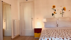Een hotelkamer met een bed, een radiator, een deur en een muur met een rookverbodsbord.