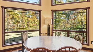 A dining room with a round table and four chairs, large windows with a view of autumn trees, and a floor lamp. - Chimney Mountain Chalet - Spacious Pet Friendly Chalet for the Whole Family (Sautee Nacoochee)