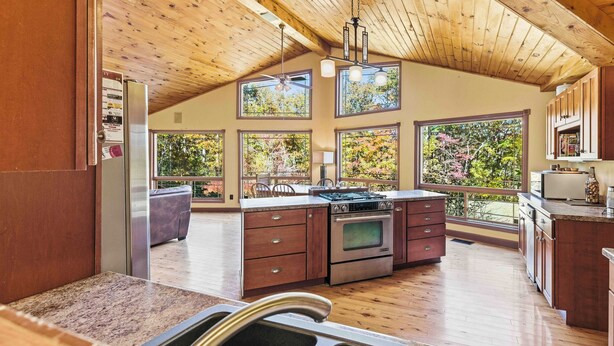 A spacious kitchen with wooden beams, large windows, and a central island with a stove. - Chimney Mountain Chalet - Spacious Pet Friendly Chalet for the Whole Family (Sautee Nacoochee)