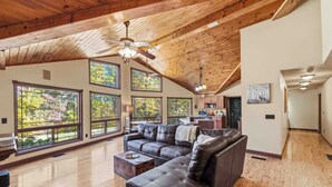 A spacious living room with a large sectional sofa, wooden flooring, and large windows offering views of trees. - Chimney Mountain Chalet - Spacious Pet Friendly Chalet for the Whole Family (Sautee Nacoochee)