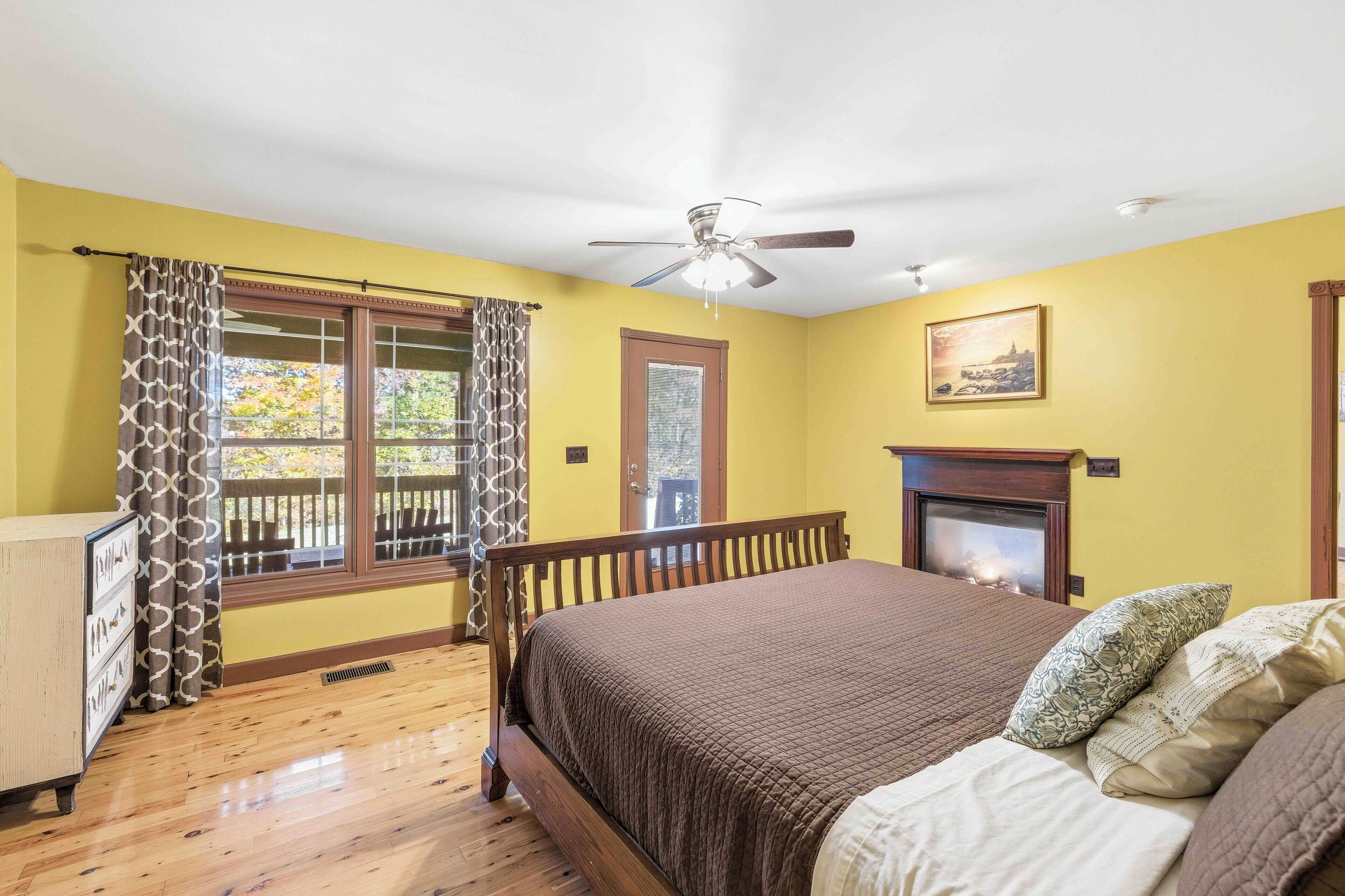 Quarto com cama, ventilador de teto, lareira e janela com cortinas.