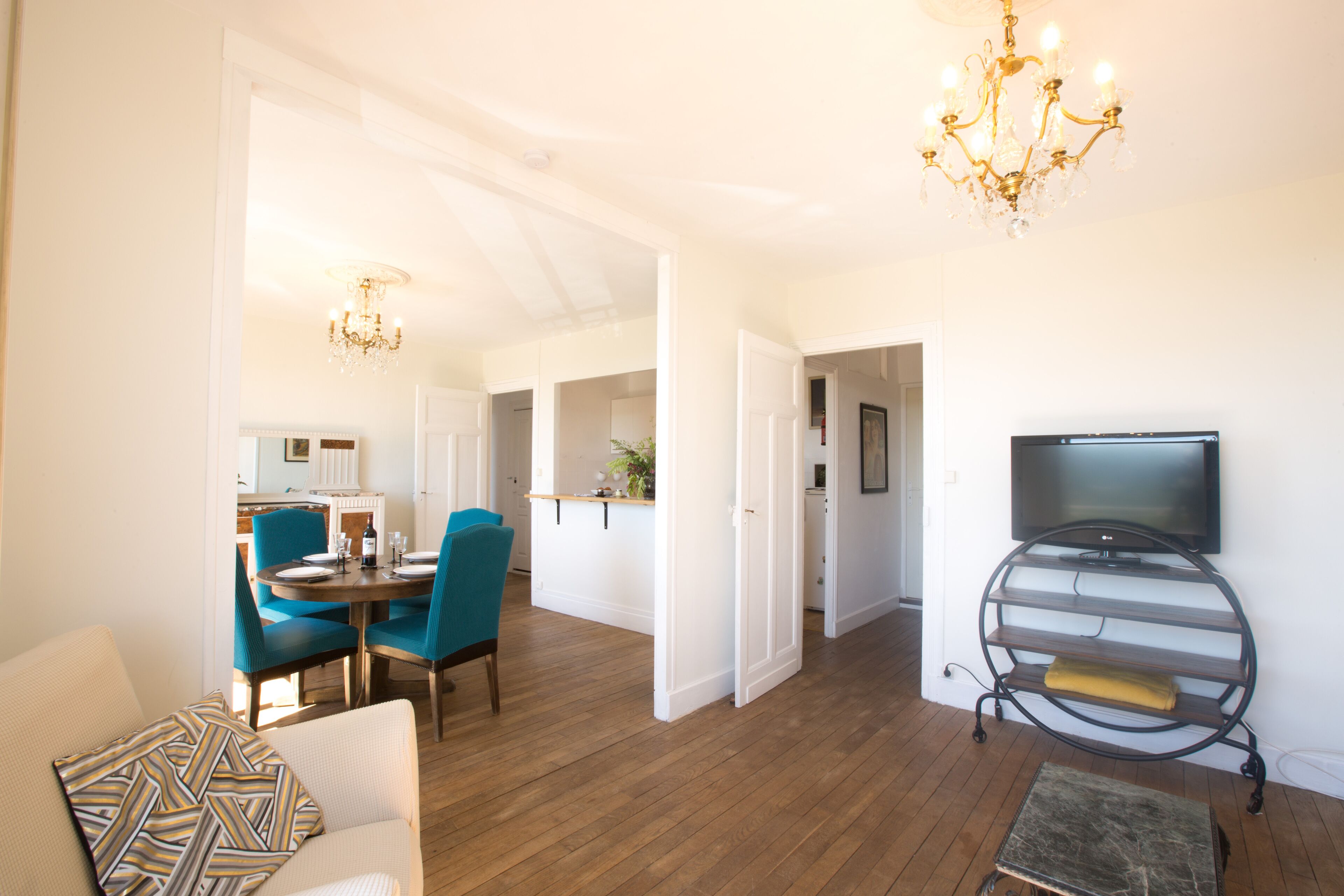 A spacious living room with a dining area, a television on a stand, and a chandelier.