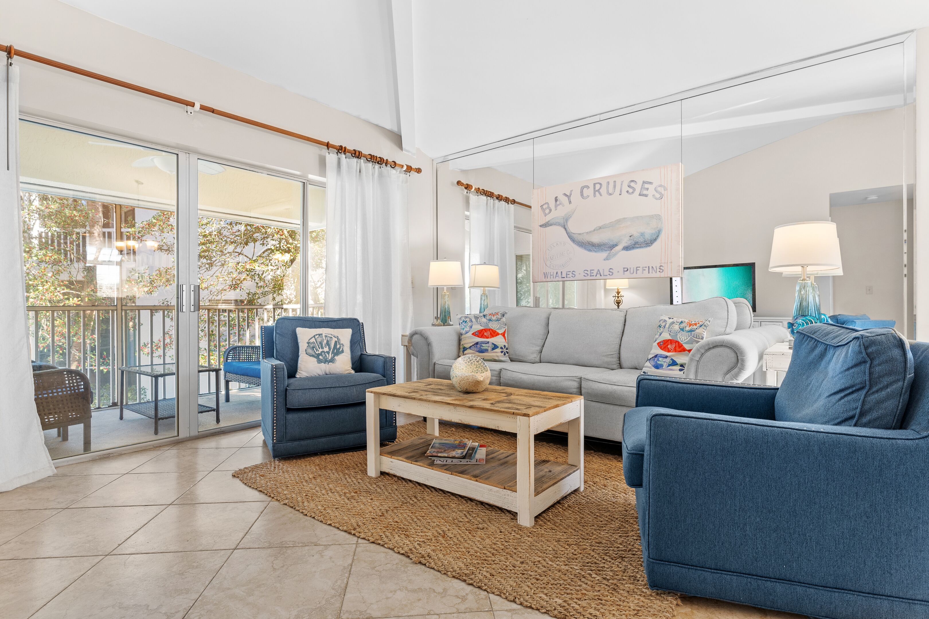 A living room with a sofa, armchairs, a coffee table, and a large window overlooking a balcony.