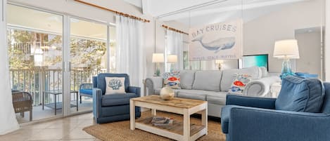 A living room with a sofa, armchairs, a coffee table, and a large window overlooking a balcony.