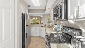 A modern kitchen with white cabinets, stainless steel appliances, and a large window providing natural light. - 2BR Beach Villa w/6-Seat GOLF CART! Near Pool, Tram, Beach. Screened Balcony (Miramar Beach)