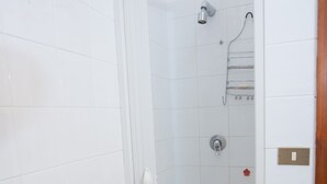 Une douche avec une porte en verre, des murs recouverts de carreaux blancs et un cadre de porte en bois.