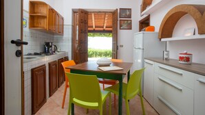 Une cuisine avec des meubles de rangement en bois, une table à manger avec des chaises, un réfrigérateur et une fenêtre donnant sur un paysage verdoyant.