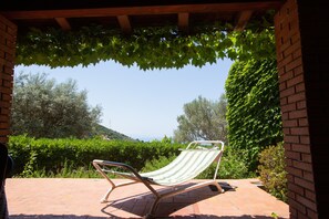 Eine Hängesessel unter einer Pergola mit Weinranken, mit Blick auf einen angelegten Garten und einen klaren Himmel.