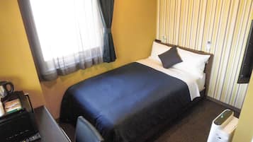 Una habitación de hotel con una cama, un escritorio con computadora, una silla y un cesto de basura.