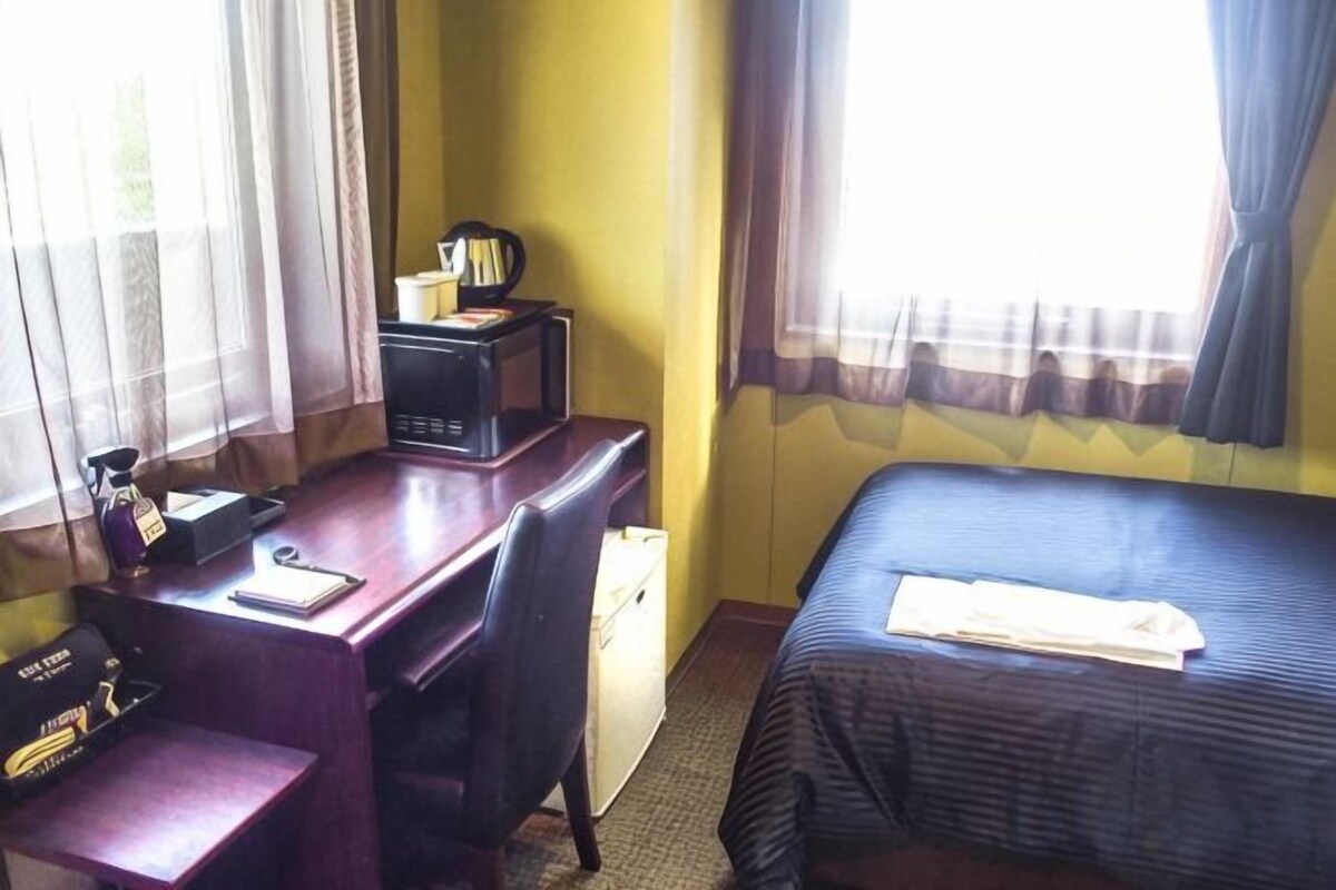 Una habitación de hotel con escritorio, cama y ventana con cortinas.