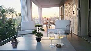 A balcony with two white chairs, a small table with a potted plant, two wine glasses, and a decorative item. - Villa Merilusi – Luxury Villa, Private Pool & Sea View (siracusa)