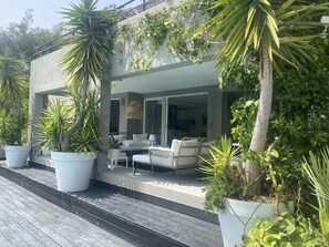 A modern outdoor seating area with white furniture and large potted plants.